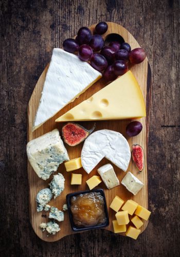 Cheese plate served with grapes, jam and figs on a wooden background