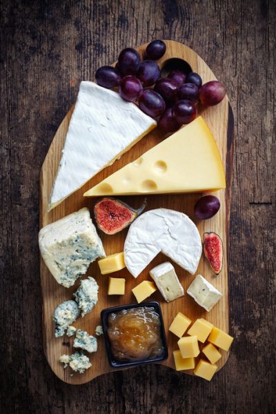 Cheese plate served with grapes, jam and figs on a wooden background